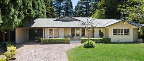 A single-story house with a covered porch, a brick driveway, and a well-maintained lawn.