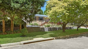 A residential building with a stone retaining wall, a grassy lawn, and mature trees.