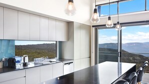 Une cuisine moderne dotée d’un grand îlot central, de meubles blancs et offrant une vue sur un paysage montagneux grâce à de larges fenêtres.