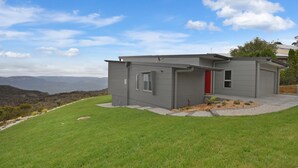 Une maison moderne avec une porte rouge, un garage et une vue sur les montagnes.