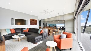 Un salon moderne avec un canapé d’angle, une table basse et un coin repas, la cuisine étant visible au fond.