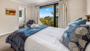 Ein Schlafzimmer mit einem großen Bett, Blick ins Freie und einem durch eine geöffnete Tür einsehbaren Badezimmer.
