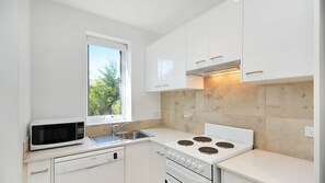 Compact kitchen with modern design, white cabinetry, and large window, featuring a microwave, sink, and stove for quick meal preparation.