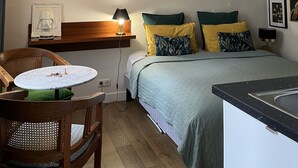 A small, cozy bedroom with a bed, bedside table, and a chair. There is a wall-mounted shelf with a framed picture and a Star Wars helmet. - Le Haut Marais, rue Notre-Dame de Nazareth (Paris)