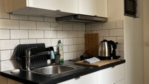 A modern kitchen with white cabinets, a black countertop, a stainless steel sink, a kettle, and a microwave. - Le Haut Marais, rue Notre-Dame de Nazareth (Paris)