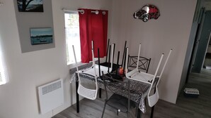 A dining area with a table and chairs, a window with a red curtain, and artwork on the walls.
