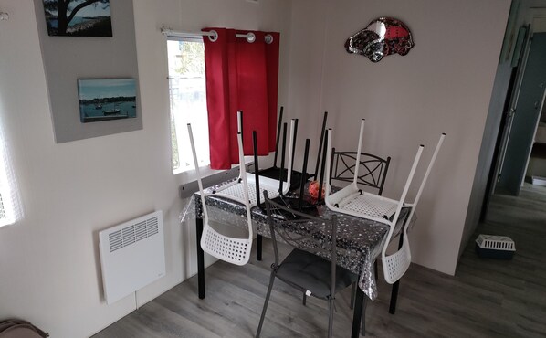 A dining area with a table and chairs, a window with a red curtain, and artwork on the walls.