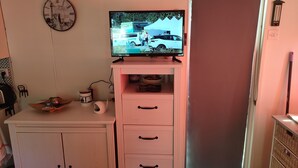 A room with a television on a white cabinet, a clock on the wall, and a door leading outside.