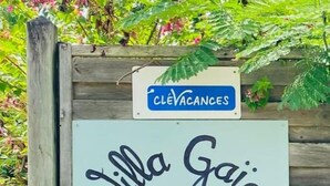 A sign for 'Villa Gaia & Bungalows' with a wooden fence and flowering plants in the background. - Villa Gaïa: Bungalow Ti-zen & spa - Parc Tropical (LE DIAMANT)
