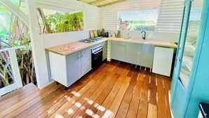 A compact kitchen with wooden flooring, white cabinetry, and a built-in stove. - Villa Gaïa: Bungalow Ti-zen & spa - Parc Tropical (LE DIAMANT)