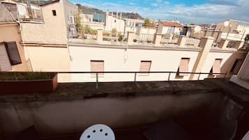 Un balcón con una silla blanca, una pequeña mesa y vistas a edificios vecinos y una colina.