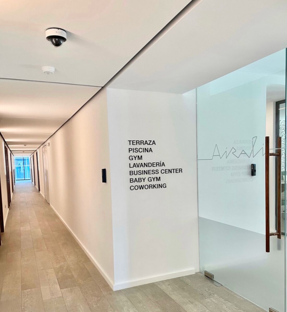 Un pasillo moderno con pared blanca que enumera comodidades como terraza, piscina, gimnasio y espacio de coworking.
