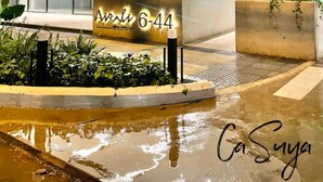 Un edificio moderno con facciata in vetro, un cartello con la scritta “Ari 6-44” e terreno bagnato che suggerisce pioggia recente.