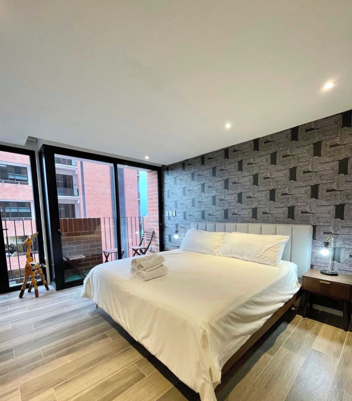 Un dormitorio moderno con una cama grande, un papel tapiz estampado y vistas al exterior.