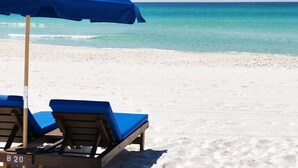 Una playa con dos sillas reclinables azules y una sombrilla azul. Se identifica como 'EDGEWATER BEACH & GOLF RESORT'.