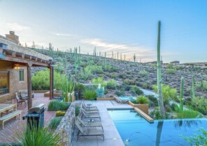 Un espace piscine aménagé avec des chaises longues, une pergola et une vue sur un paysage désertique.