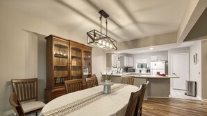 Un comedor con una mesa redonda, sillas de madera, una araña y una cocina al fondo.