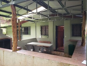 A covered outdoor area with a table and chairs, a trash bin, and a door leading to another room. - Naturist's Paradise (Guadalajara Rio Piedras)