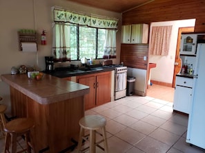 A compact kitchen with wooden cabinets, a central island, a stove, and a refrigerator. - Naturist's Paradise (Guadalajara Rio Piedras)