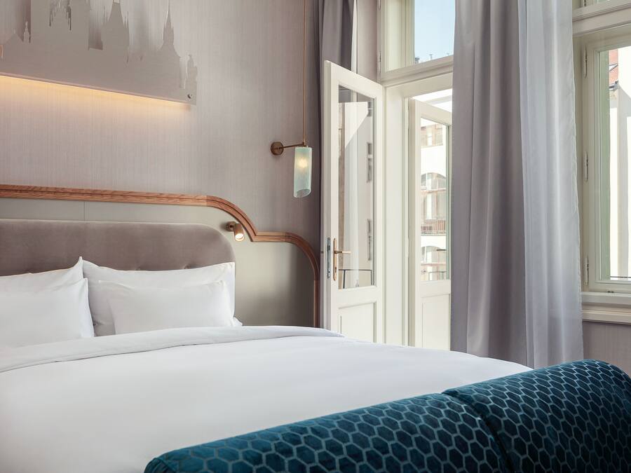 A hotel room with a large bed, a wooden headboard, a wall-mounted light fixture, and a window with curtains.