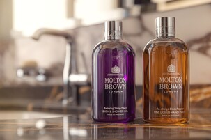 Two bottles of Molton Brown bath and shower gel on a reflective surface.