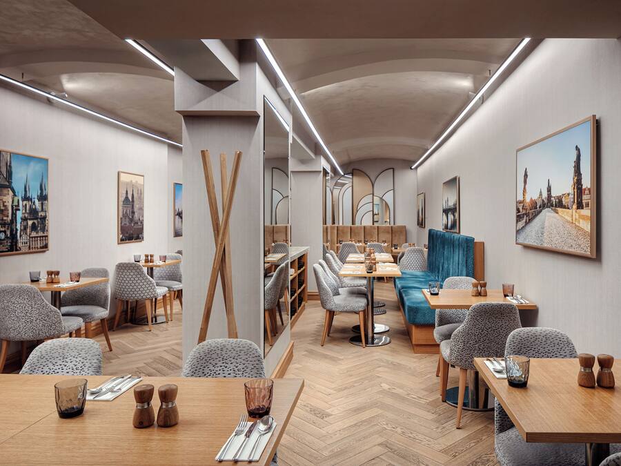 A modern restaurant with wooden tables and chairs, a herringbone floor, and cityscape paintings on the walls.