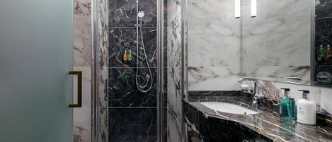 A modern bathroom with a glass-enclosed shower, a marble-tiled sink, and a large mirror.