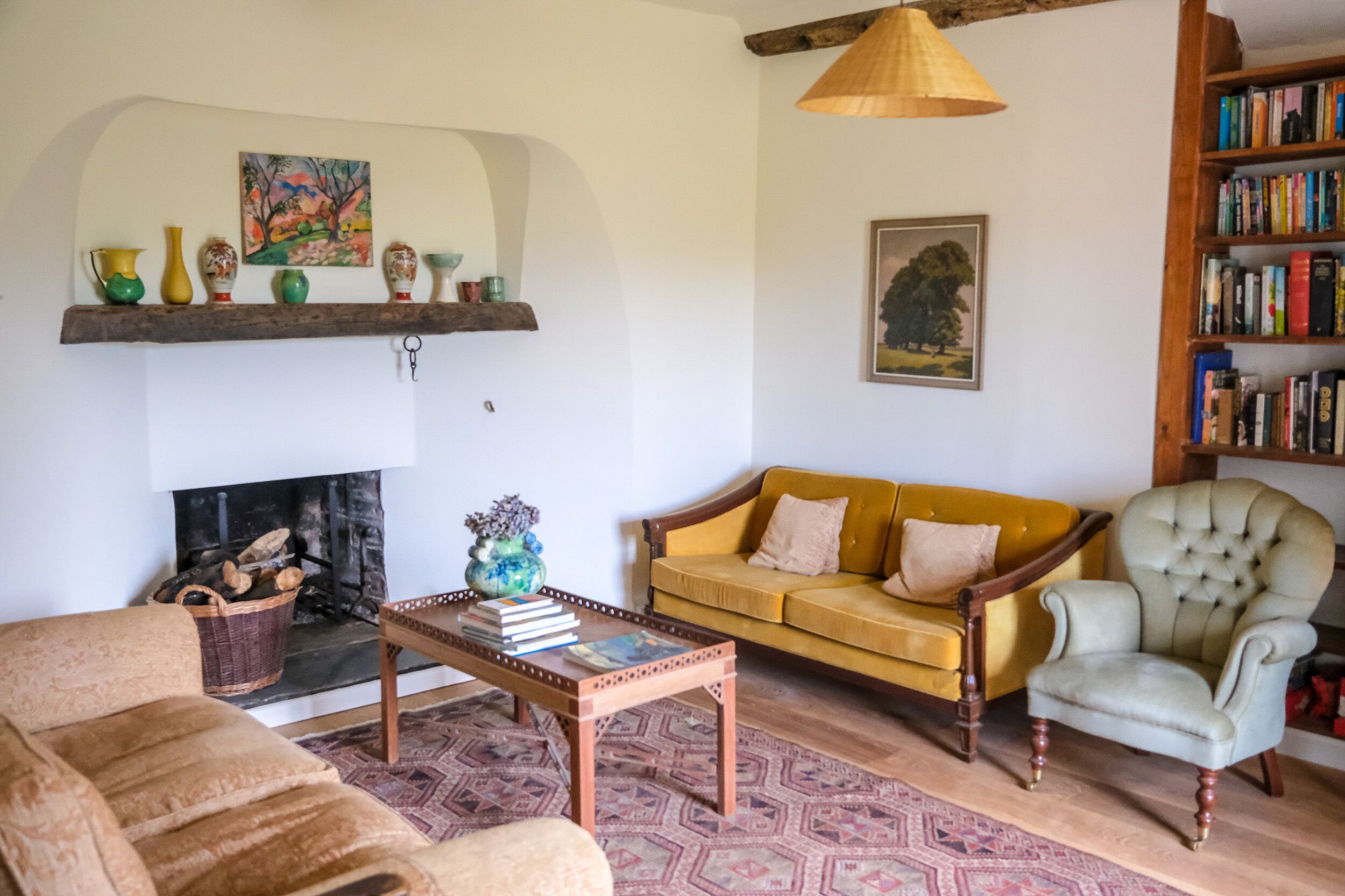 A cozy living room with a fireplace, a yellow sofa, a wooden coffee table, and a bookshelf.
