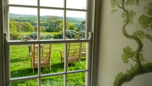 A room with a large window overlooking a grassy landscape and a mural of a tree. - Henllys (Crymych)