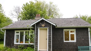 A small, dark-colored house with a gabled roof and a front door. - Henllys Lodge (Crymych)