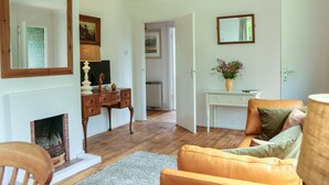 A living room with a fireplace, a wooden coffee table, a sofa, and a white desk with a vase of flowers. - Henllys Lodge (Crymych)