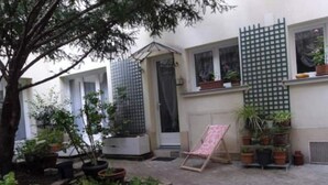 A small courtyard with a tree, potted plants, a folding chair, and a green trellis. - Haut Marais, rue Volta, 2 bedrooms, 2 bathrooms (Paris)