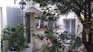 A courtyard with potted plants, a small tree, and a building with a window and door. - Haut Marais, rue Volta, 2 bedrooms, 2 bathrooms (Paris)