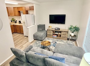 A living room with a grey sofa, a coffee table, and a TV mounted on the wall.