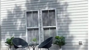 A patio with two chairs and a small table, potted plants, and a window with shutters.