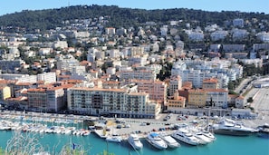 A coastal cityscape with residential buildings, a marina with yachts, and a clear blue sky.
