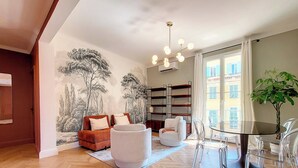 Un salon moderne avec un canapé, des fauteuils, une table en verre et une bibliothèque.