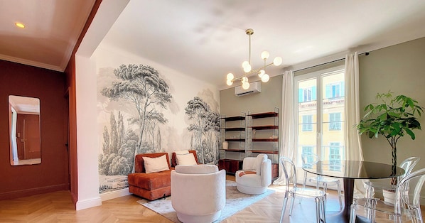 A modern living room with a sofa, armchairs, a glass table, and a bookshelf.