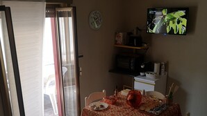 A dining area with a table set for two, a television mounted on the wall, and a sliding glass door leading to an outdoor area. - Private apartment (Chianchitta)