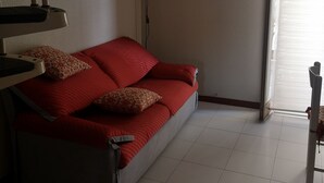 A living room with a red sofa, a painting on the wall, an air conditioning unit, and a window with blinds. - Private apartment (Chianchitta)