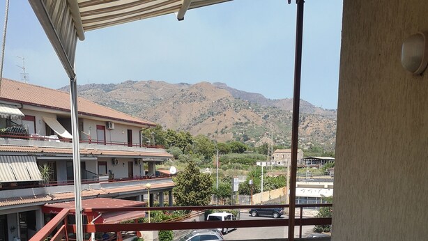 A covered outdoor seating area with a round table and white plastic chairs, overlooking a mountainous landscape. - Private apartment (Chianchitta)