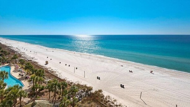 Una spiaggia con piscina, palme e cielo sereno.