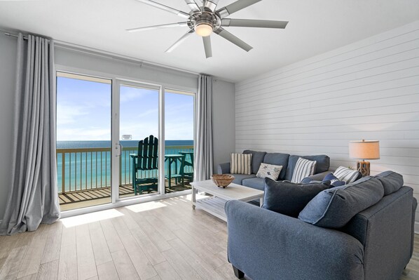 A modern living room with a grey sofa, a white coffee table, and a ceiling fan. - Welcome to 707 West! GULFFRONT with Free Beach Service and Activities! (Panama City Beach)