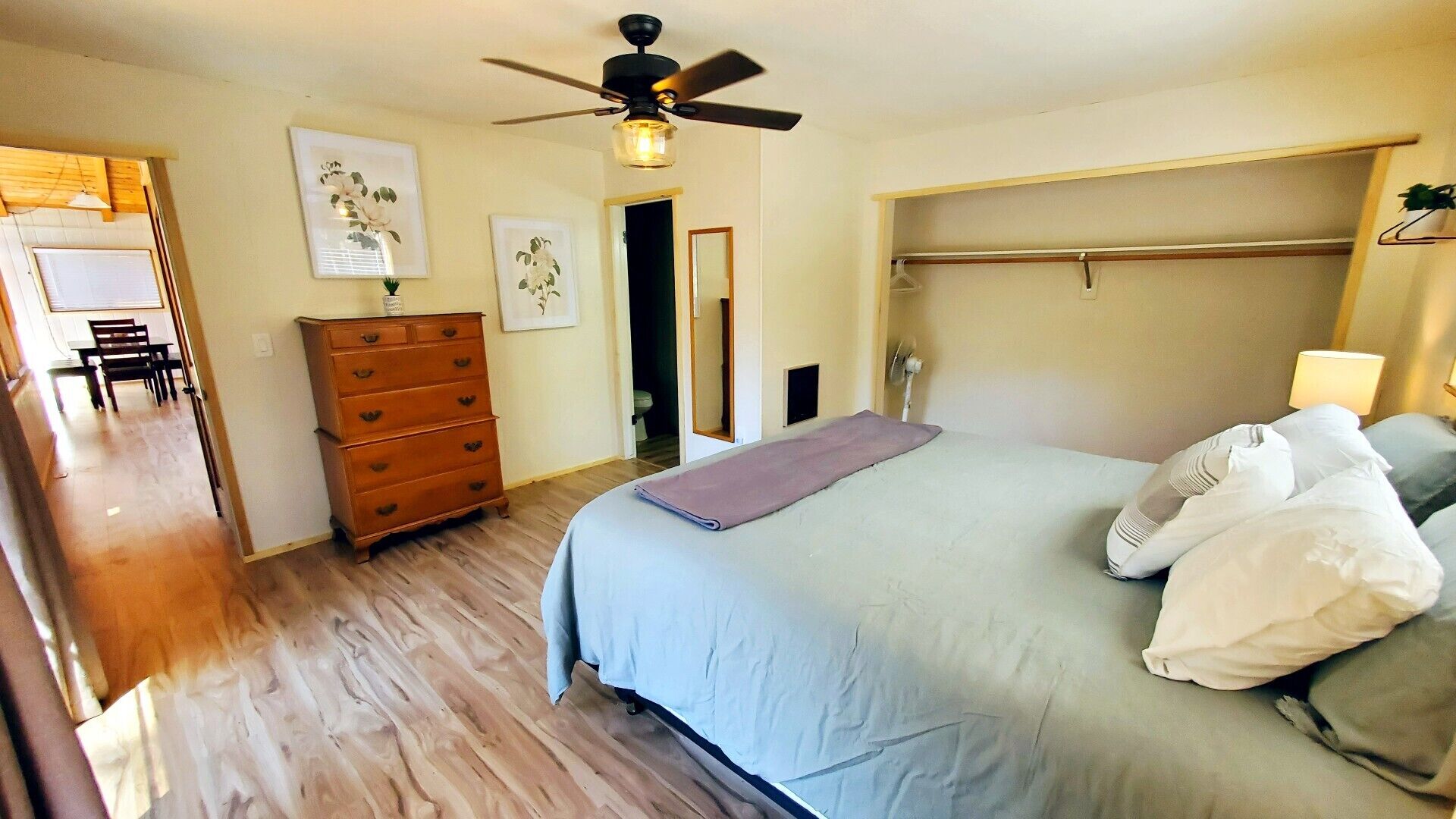 A bedroom with a bed, a dresser, a ceiling fan, and a door leading to a bathroom.