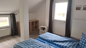 Ett sovrum med ett sluttande tak, en säng med blått, rutigt sänglinne, ett litet nattduksbord med en växt och ett fönster med gardiner.