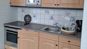 Ett kök med träskåp, en mikrovågsugn, ett handfat och en klocka på väggen.