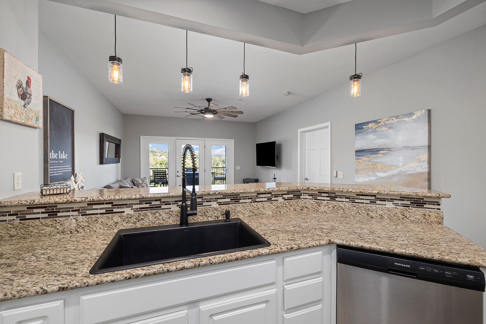 A modern kitchen with granite countertops, a black sink, white cabinetry, a dishwasher, and a ceiling fan.