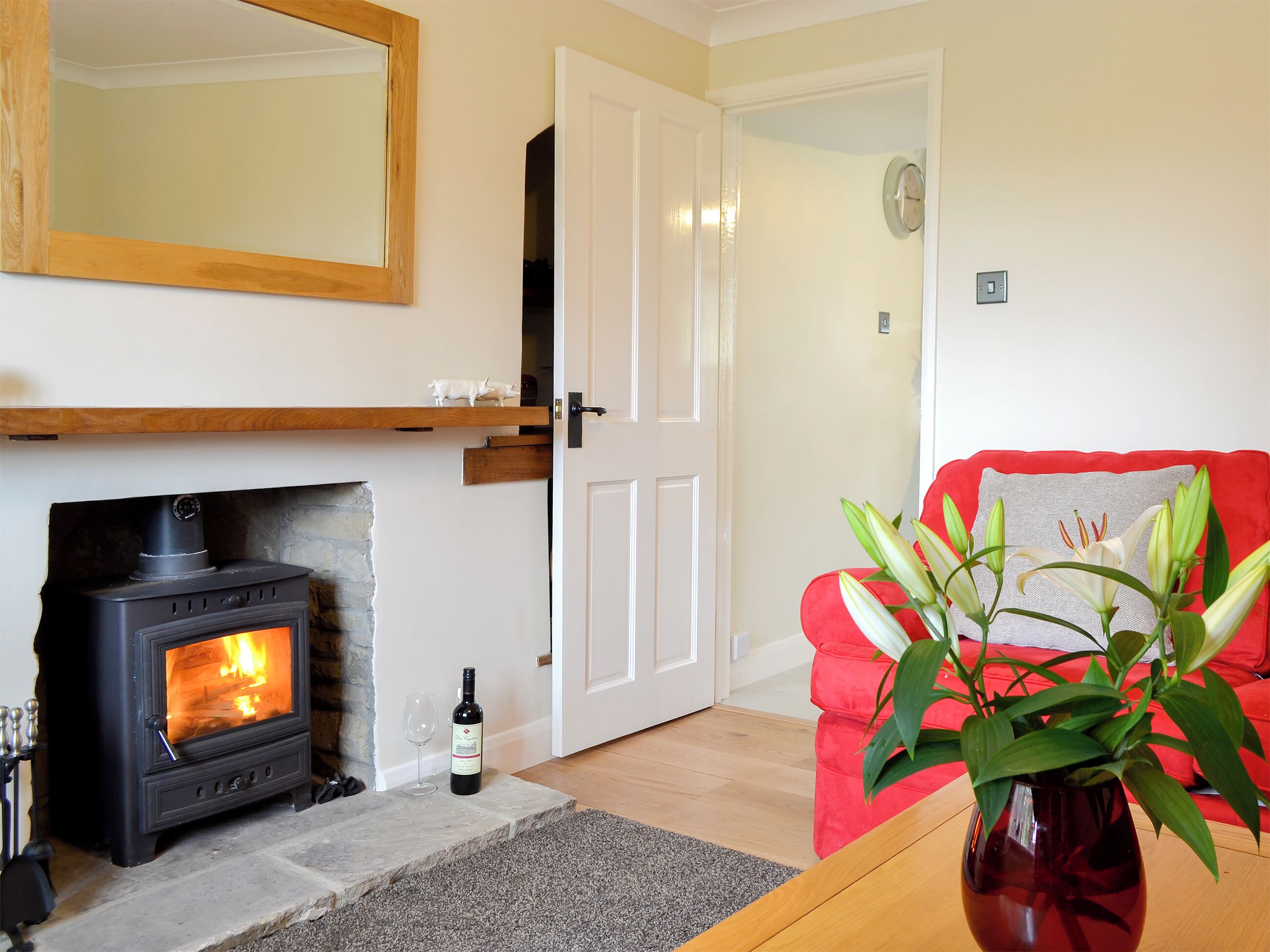 A cozy living room with a fireplace, a red couch, a wooden coffee table, and a vase with flowers.