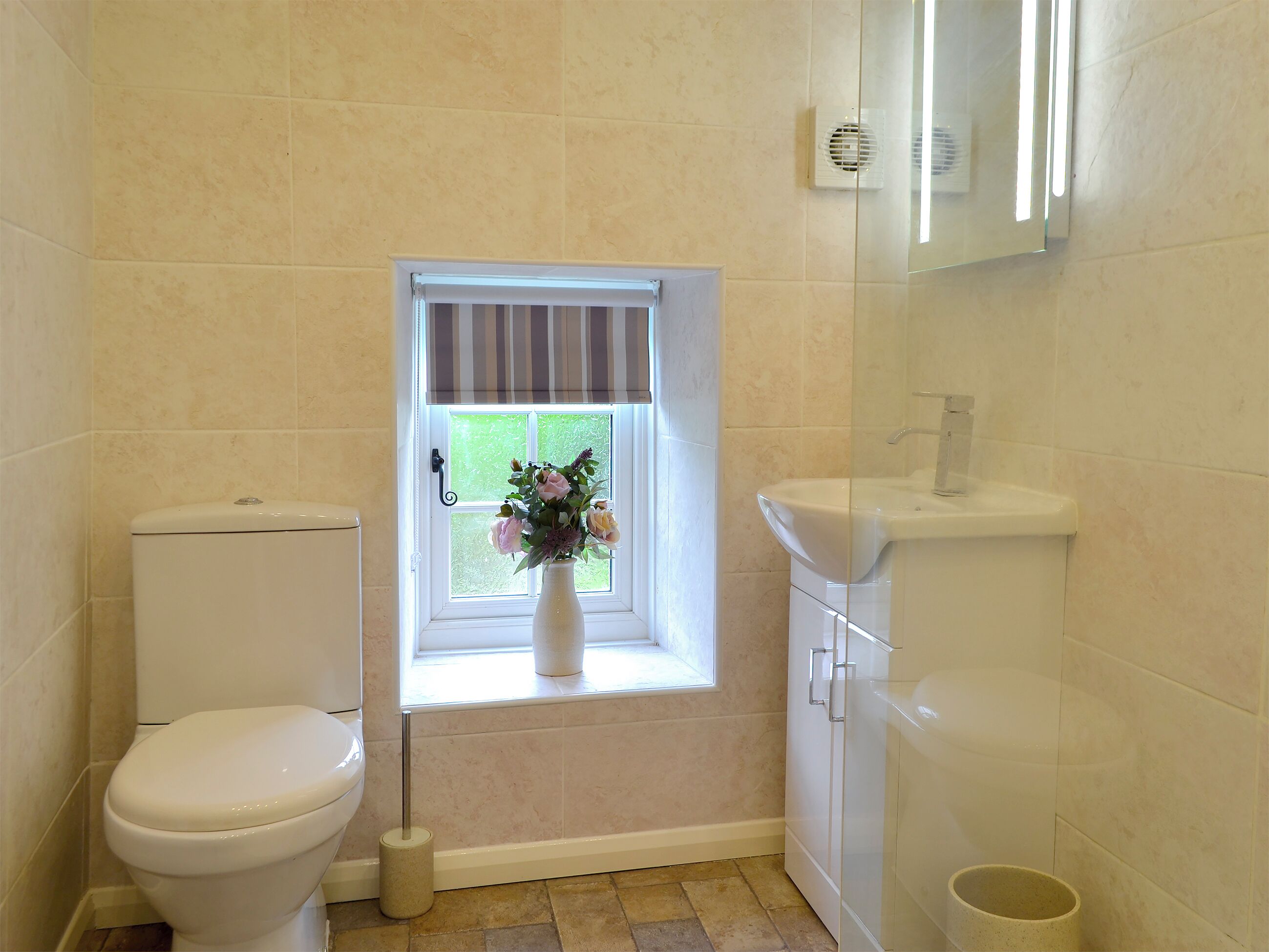 Une petite salle de bain avec des toilettes, une fenêtre donnant sur un beau paysage, un lavabo et un miroir.