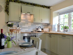 A kitchen with light green cabinets, a tiled backsplash, a stove, a toaster, and a window with a view of greenery.